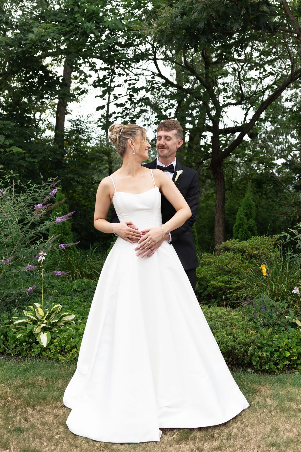 Elegant wedding couple in white dresses pose together in a lush garden setting.