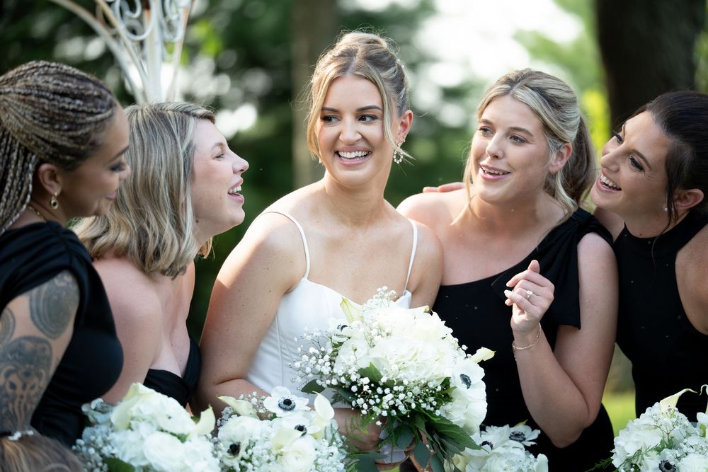Wedding party in black dresses sharing laughs together outdoors.