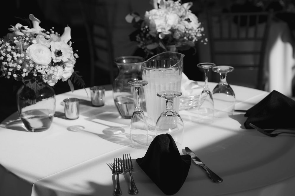 A black and white panoramic photograph of an elegant wedding reception table setting with floral centerpieces and linens.