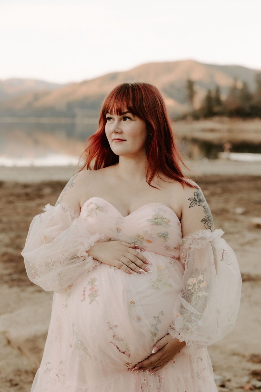 A person in a flowing white dress poses against a desert landscape in a dreamy maternity photoshoot series.