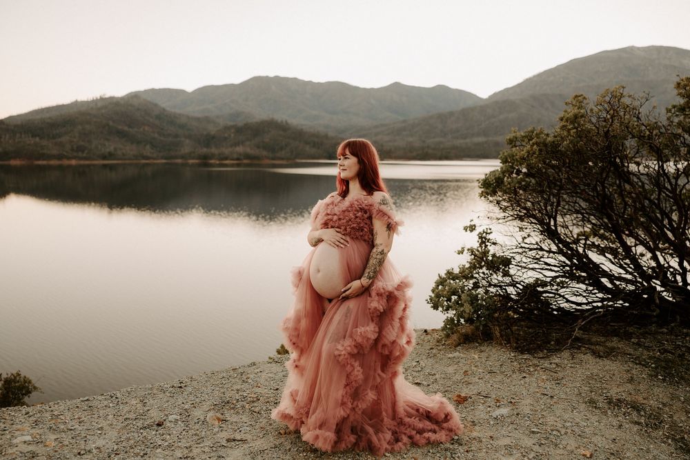 A dreamy photoshoot in a pink flowy dress by a misty lake at sunset creates an ethereal atmosphere.