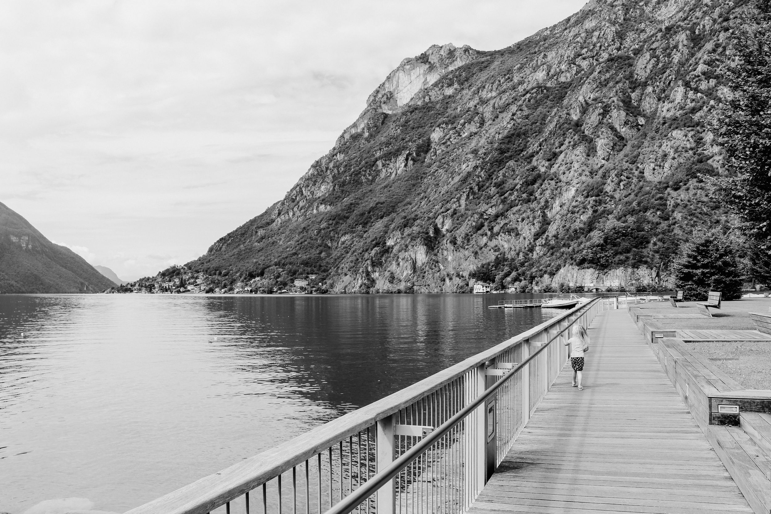 Mountain lake boardwalk extending into calm waters surrounded by steep rocky peaks.