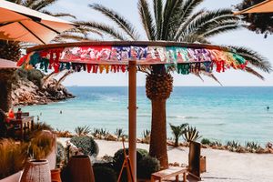 Tropical beach scene with orange umbrellas, palm trees, and turquoise ocean water.