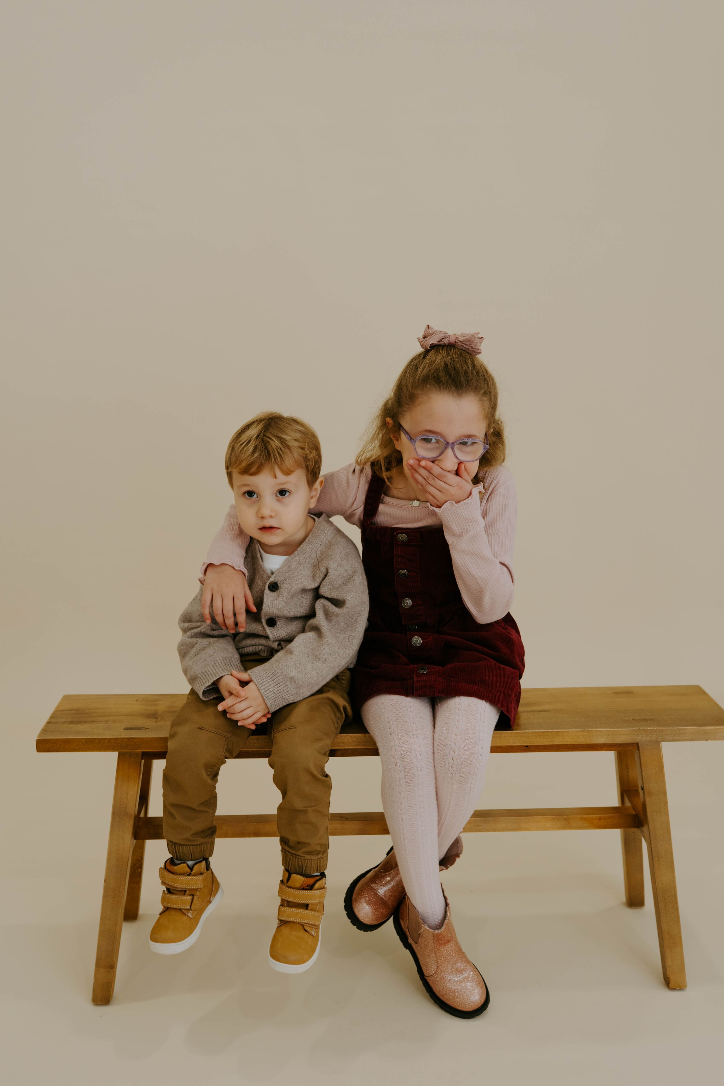 Two children sit together on wooden bench during studio photoshoot.