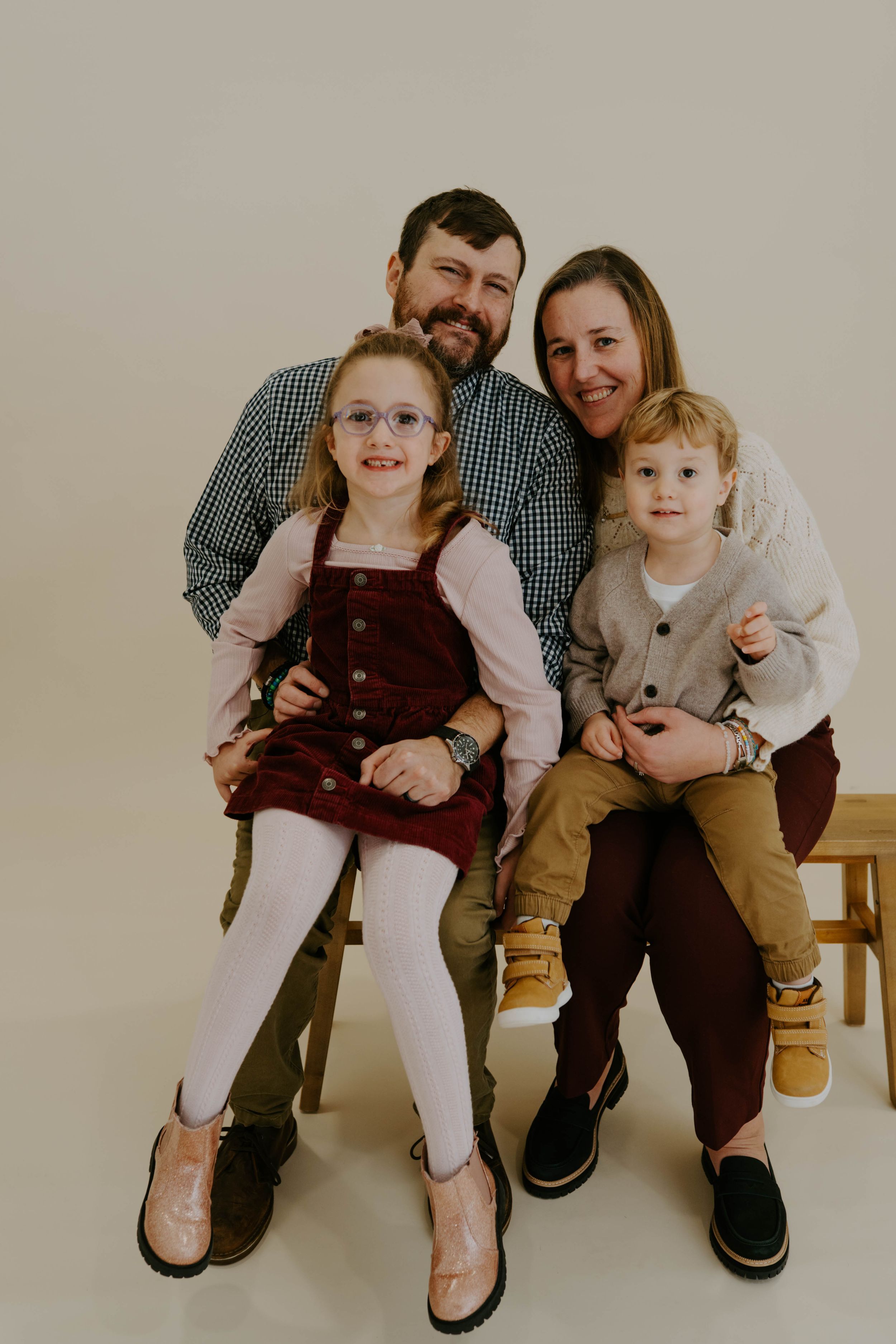 Family of four poses together on wooden bench during studio portrait session.
