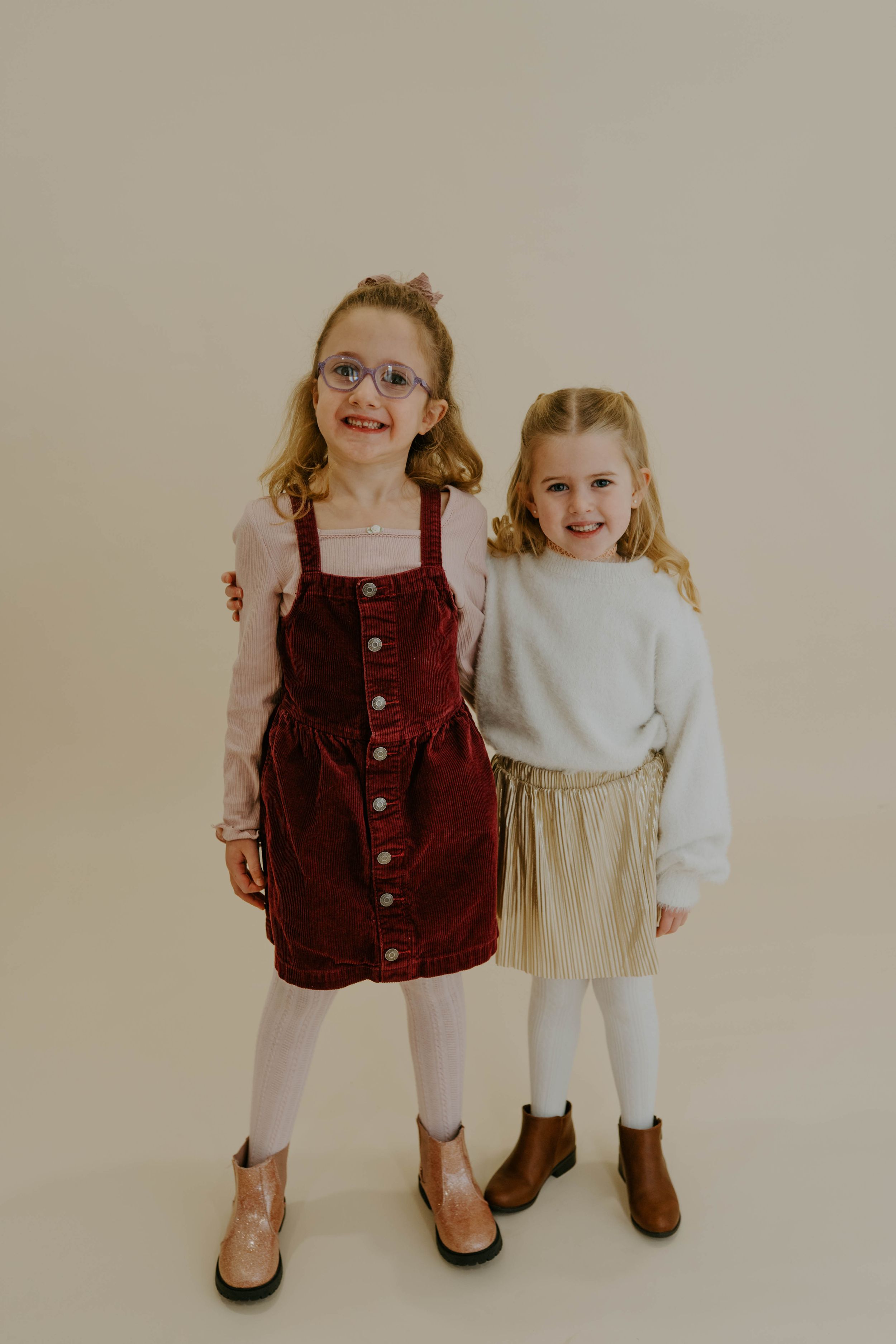 Two children smile and pose together wearing fall fashion outfits against a neutral backdrop.