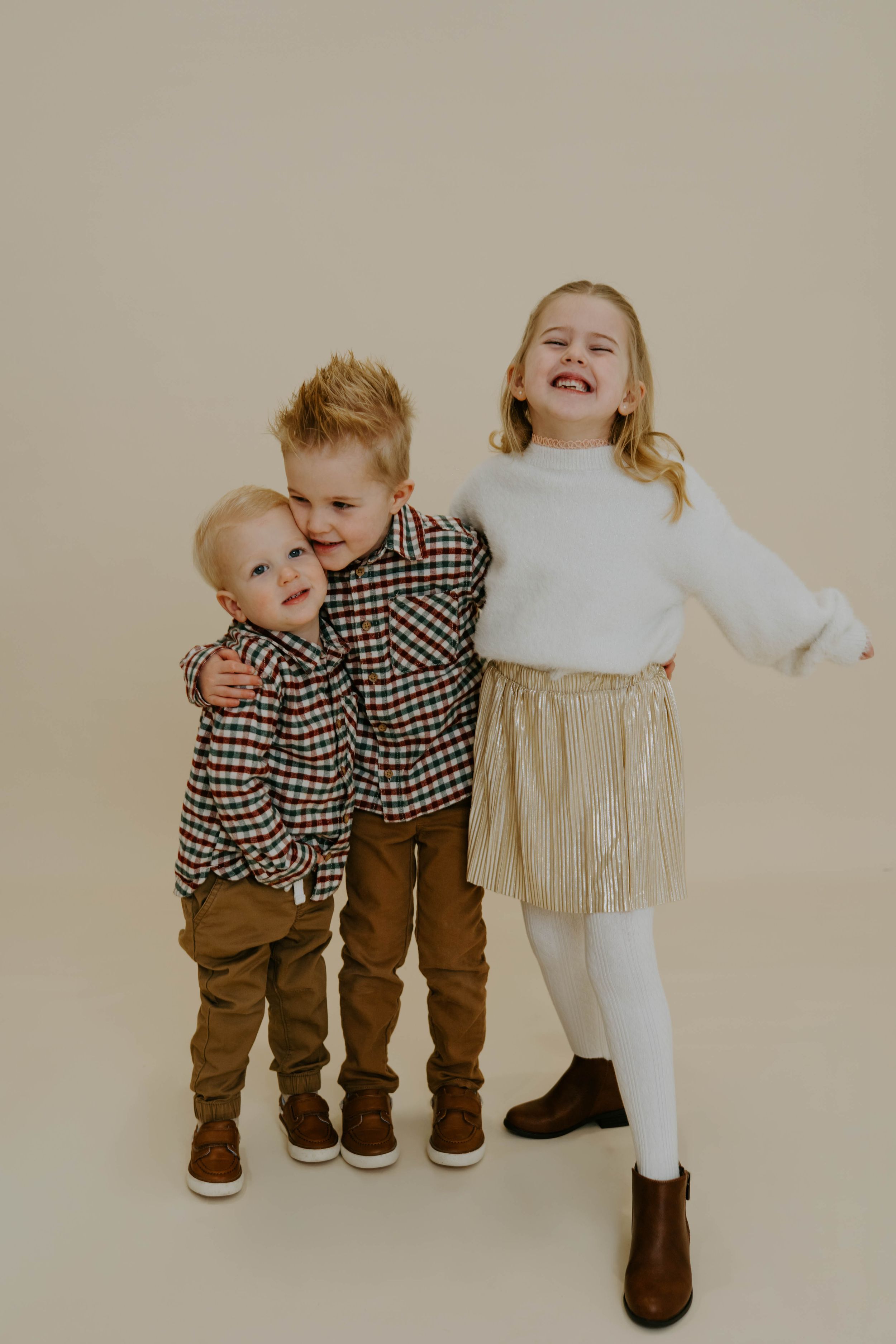 Three children pose playfully in coordinated fall outfits against beige background.