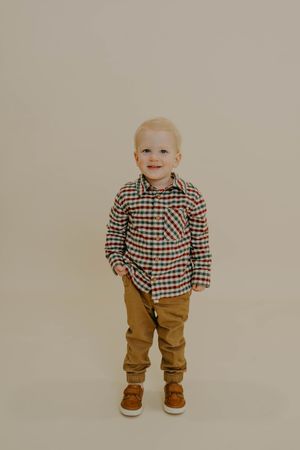Small child in plaid shirt and brown pants walking and smiling against beige background.
