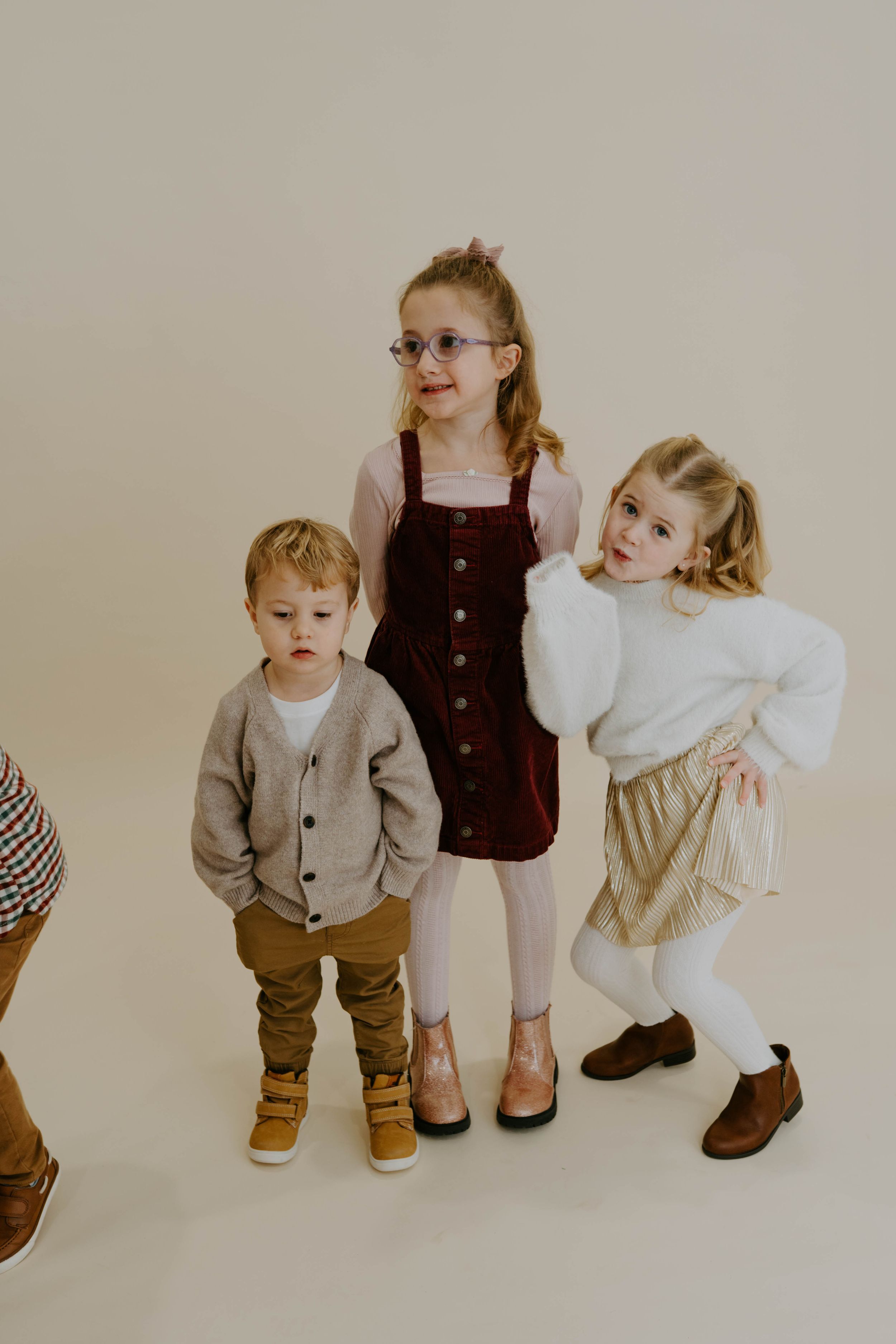 Three children pose together in coordinated autumn outfits during studio photoshoot.
