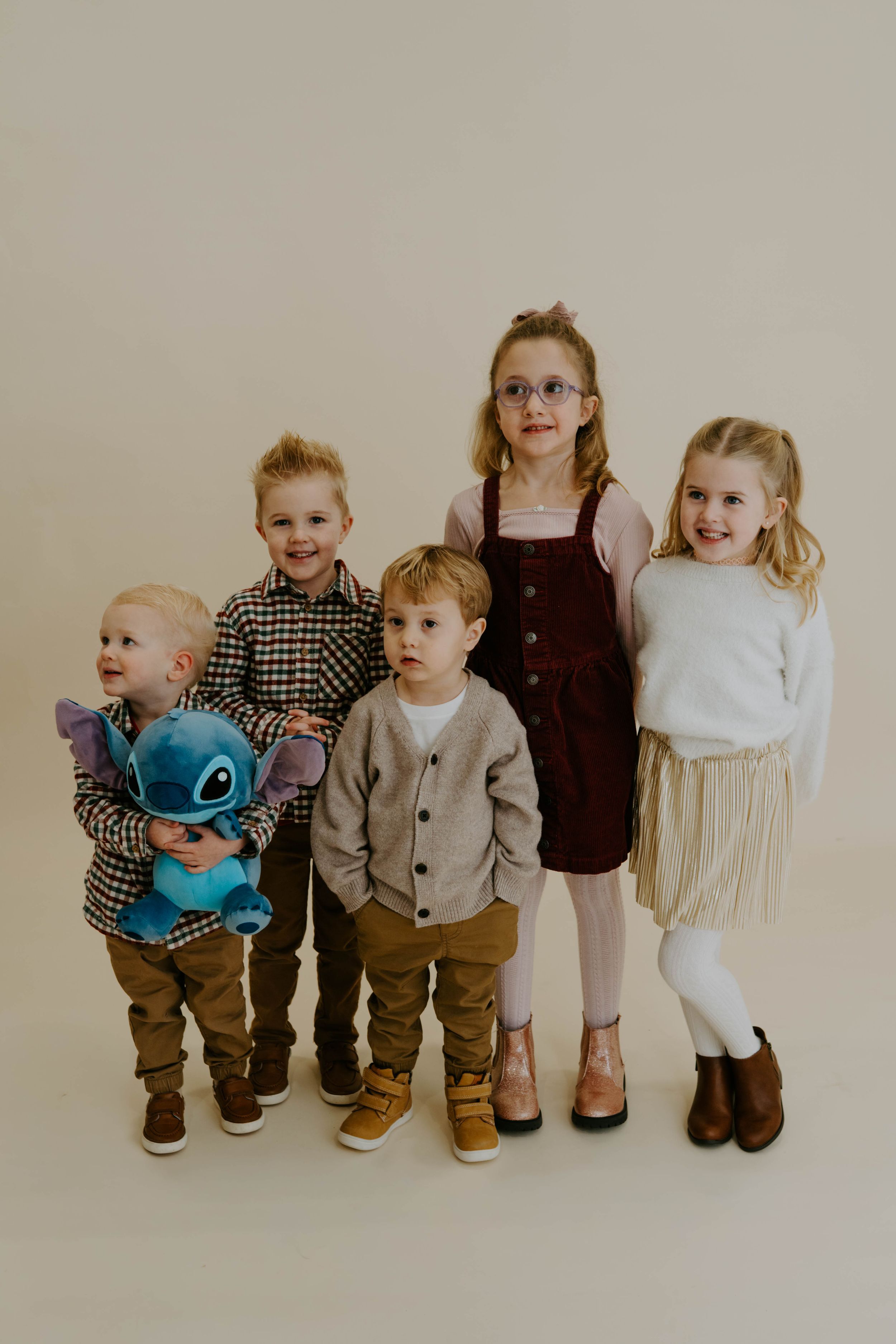 Five children line up for portrait, one holding blue Stitch plush toy, wearing coordinated casual outfits.