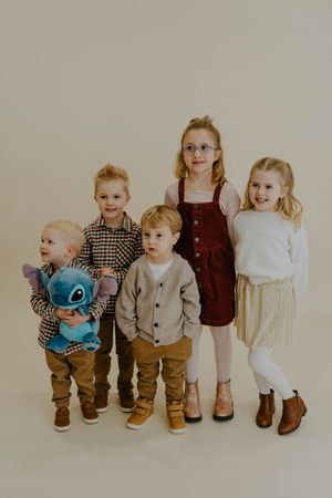 Children standing in line wearing coordinated outfits with plaid shirts and brown pants.