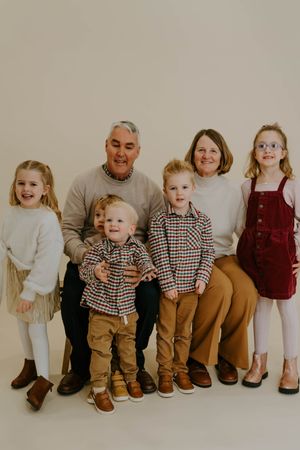 Multi-generational family portrait with coordinated neutral-toned outfits against beige backdrop.