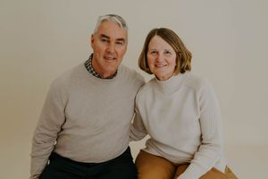Couple in matching cream sweaters pose together for portrait against neutral background.