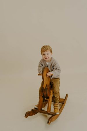 Young child playing on a wooden rocking horse against a neutral background.