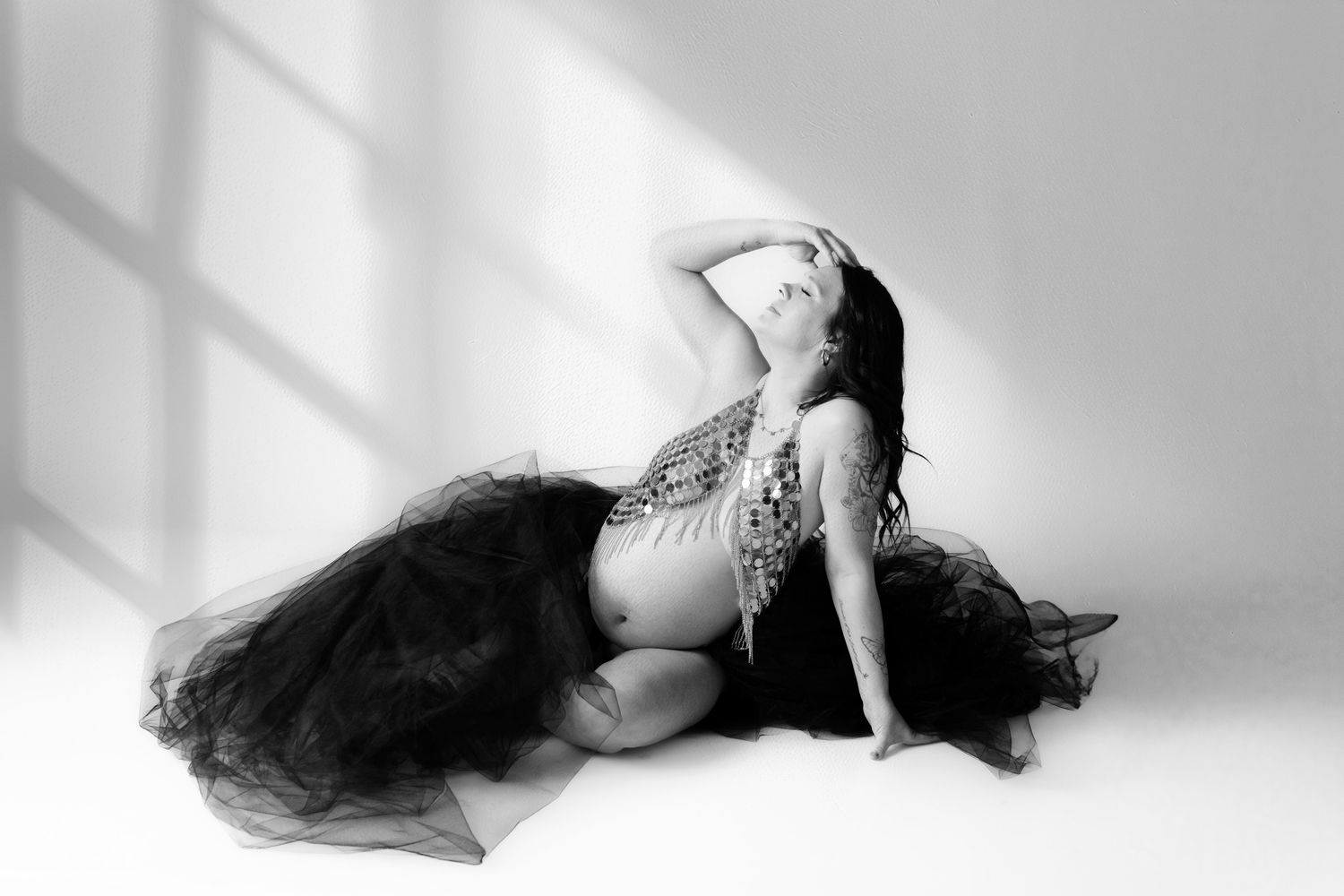 Artistic black and white boudoir photo of dancer in flowing black tulle skirt posing gracefully in window light.