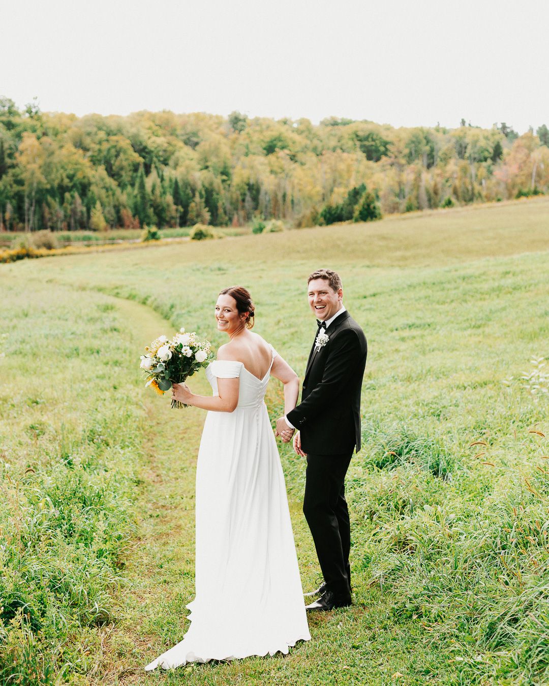 Wedding couple walking through a green meadow on their special day.