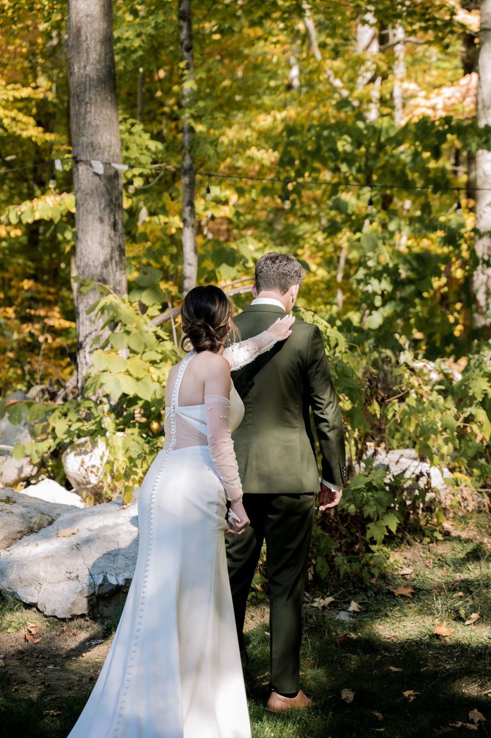 A couple shares a tender first look moment in a sunlit autumn forest setting.