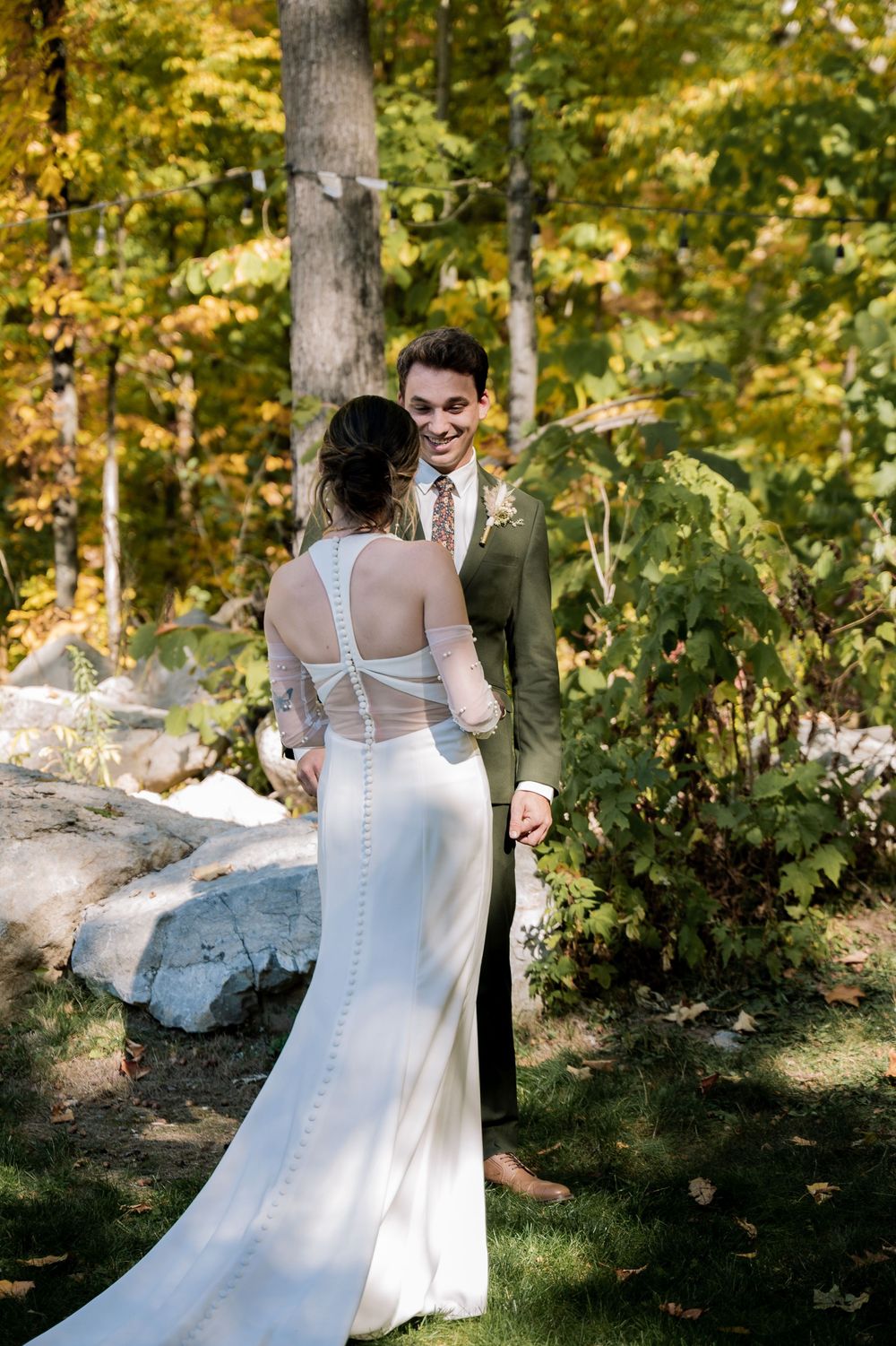 A romantic wedding moment captured in a wooded setting with autumn foliage and sunlight filtering through the trees.