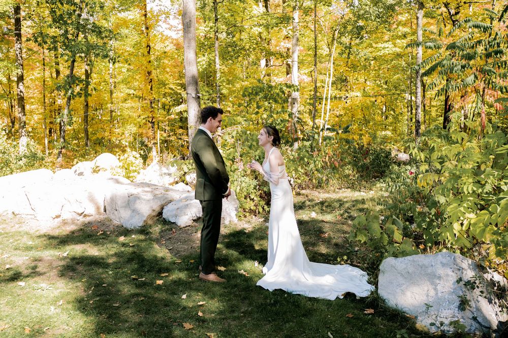 A couple in wedding attire poses in a sunlit autumn forest with golden yellow foliage creating a romantic backdrop.