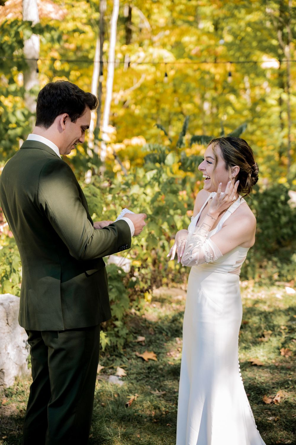 A couple shares an emotional reaction during their outdoor wedding ceremony surrounded by fall foliage.