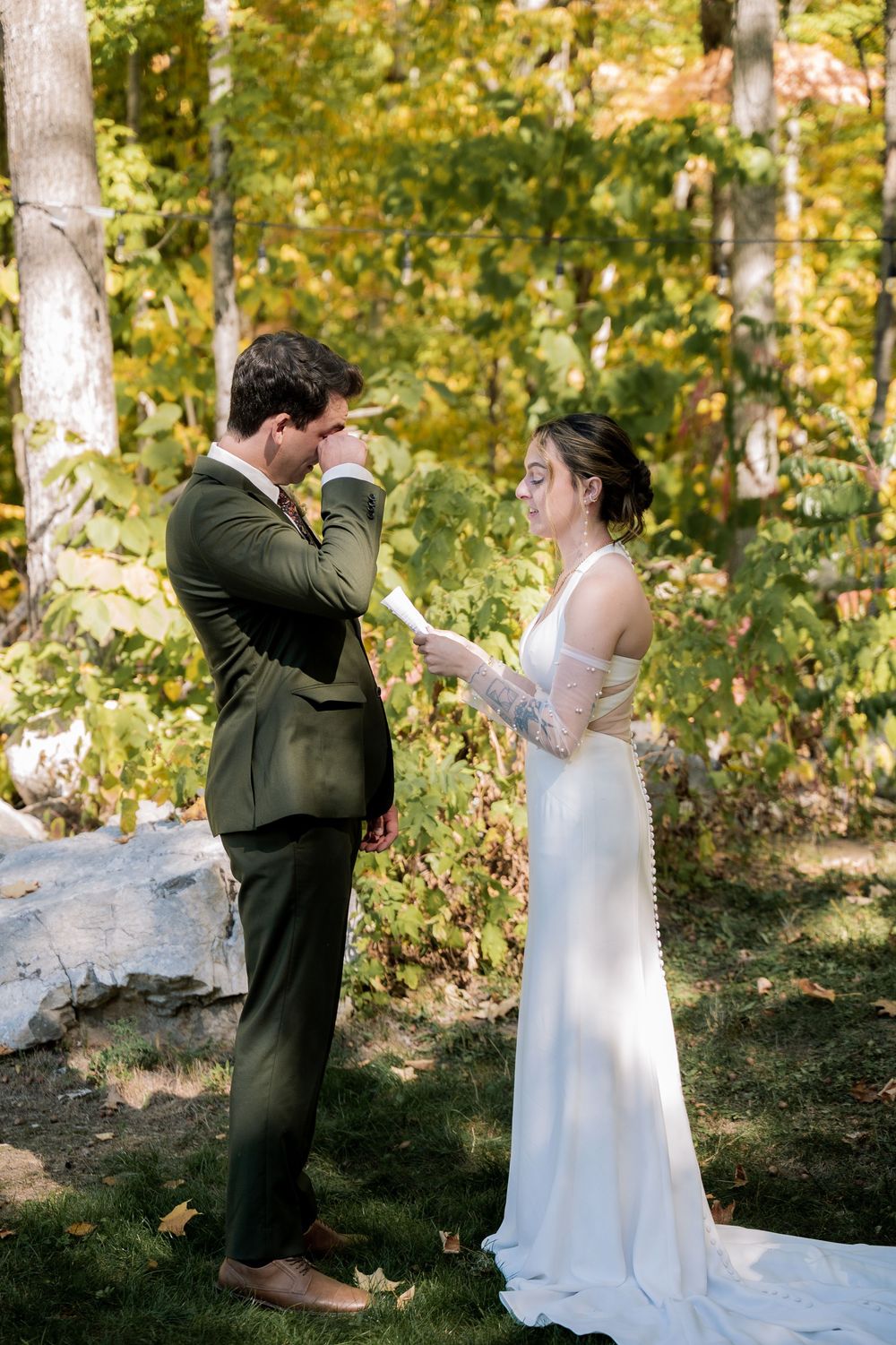 A couple shares an emotional first look moment during their outdoor autumn wedding ceremony in a wooded setting.