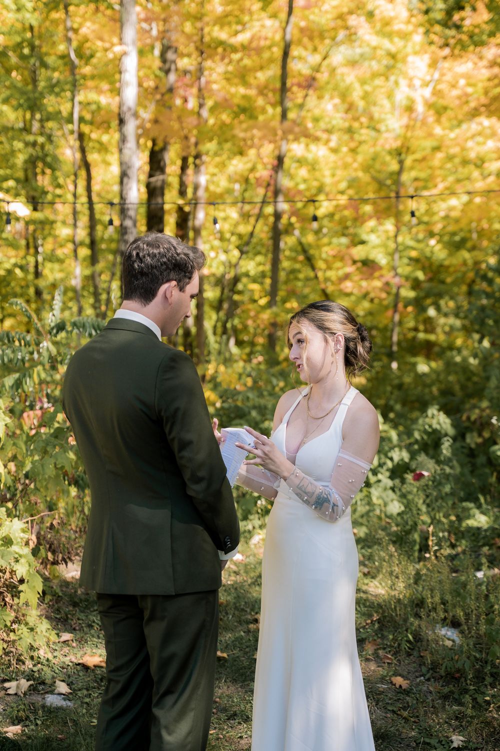 A couple exchanges vows while reading from papers in a golden autumn forest setting.