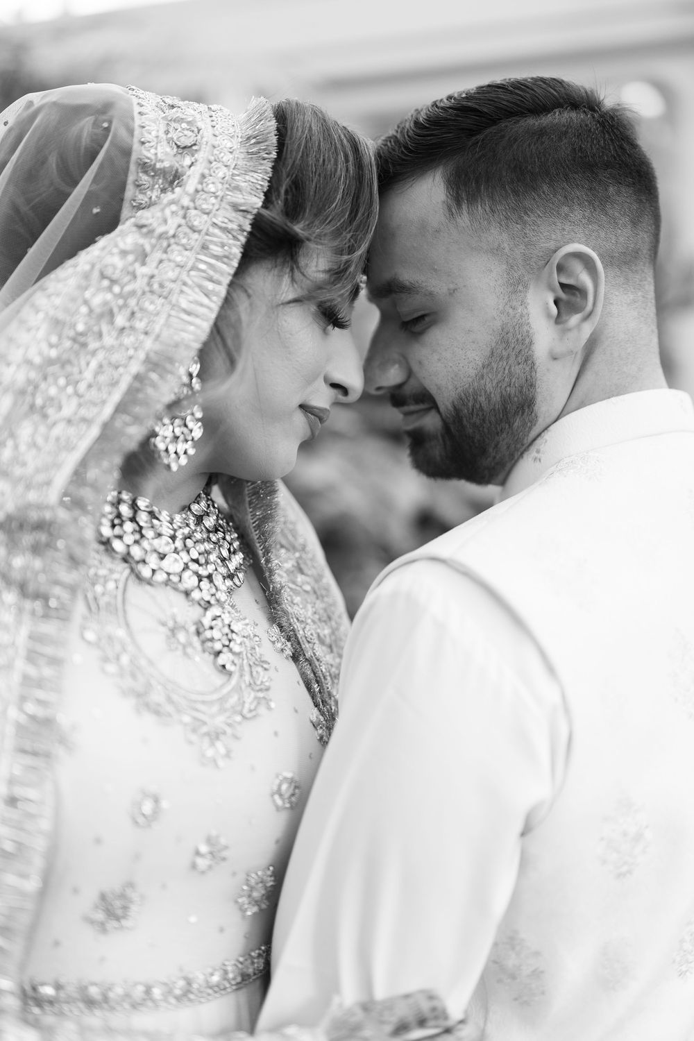 Black and white portrait of a South Asian bride and groom in traditional wedding attire touching foreheads.