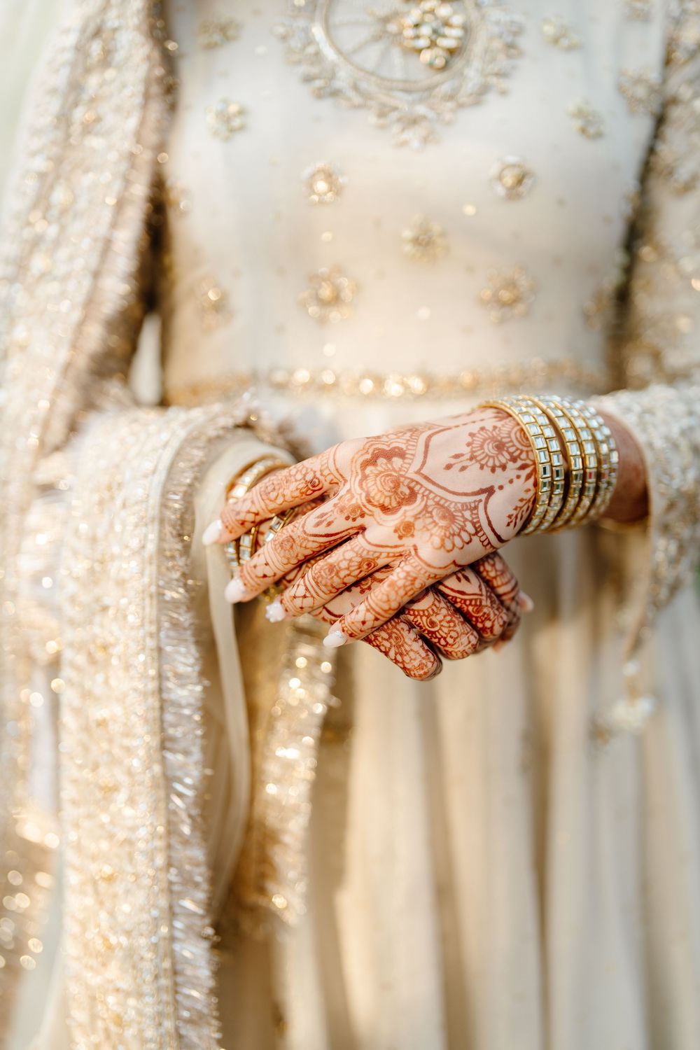 Close-up of a South Asian bride's hands adorned with intricate henna and gold bangles on her wedding day.