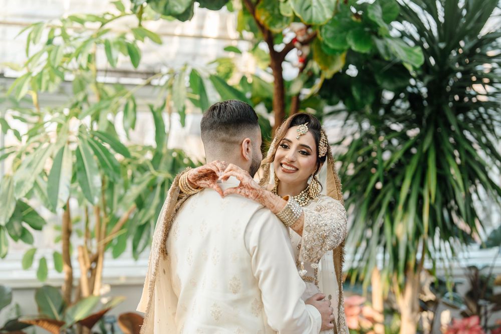 South Asian bride and groom sharing romantic moment in lush greenhouse wedding venue.
