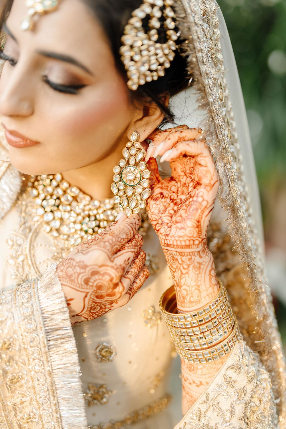 Close-up of South Asian bride with intricate mehndi hands adjusting kundan earring on wedding day.