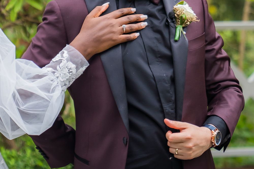 Close-up view of hands holding a wedding bouquet with white flowers against a burgundy suit jacket.
