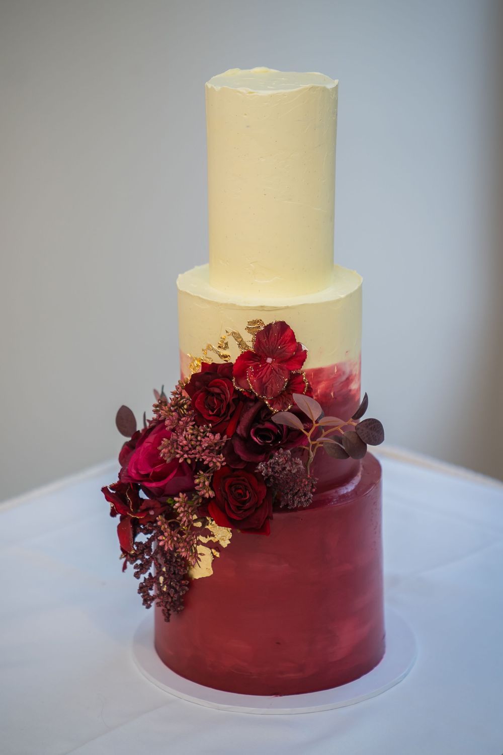Elegant two-tier wedding cake decorated with burgundy fondant base and fresh red roses in an ombre design.