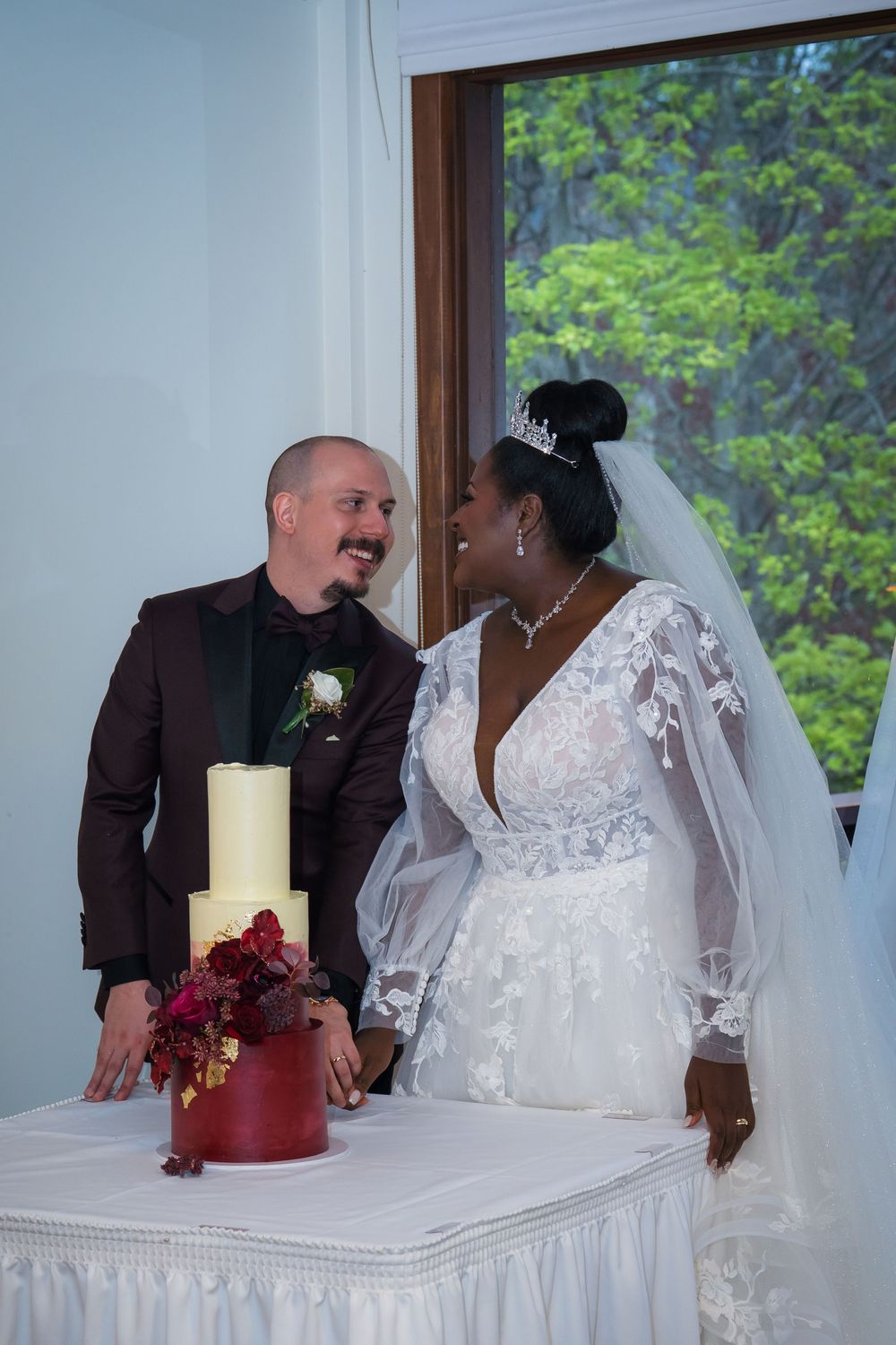 A wedding couple sits at a decorated table with a red and white floral centerpiece and candle during their reception.