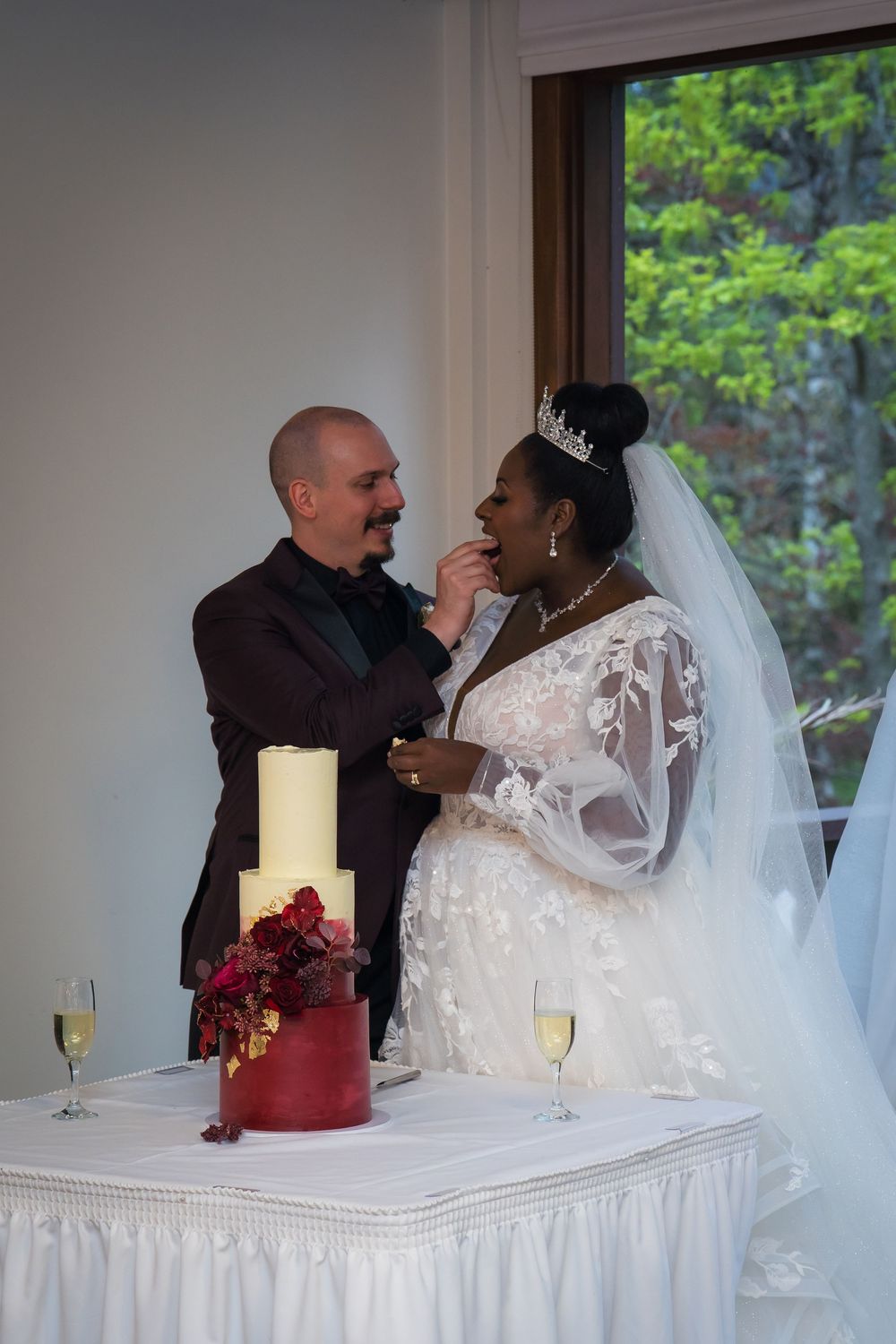 A joyful wedding couple shares a candid moment while sitting at their reception table with white linens and red decor.