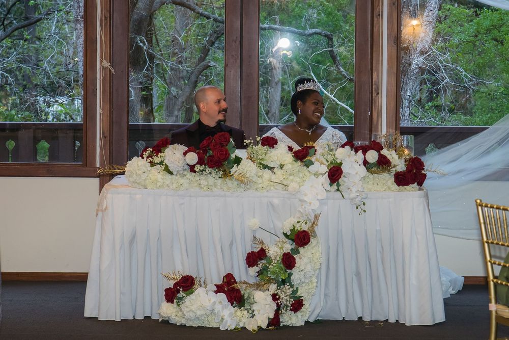Elegant wedding reception venue decorated with burgundy and white floral arrangements on white tablecloths.