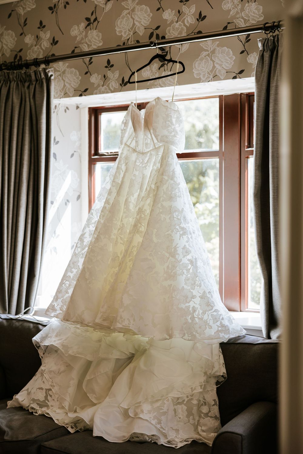White wedding dress hanging by a window with delicate lace details and flowing ruffles in natural light. Cabra Castle