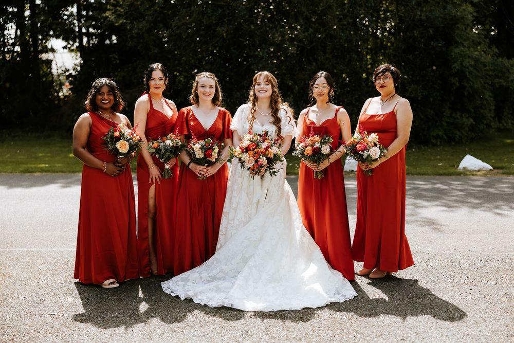 A bridal party poses outdoors wearing elegant red bridesmaid dresses alongside a bride in a white lace gown. Cabra Castle