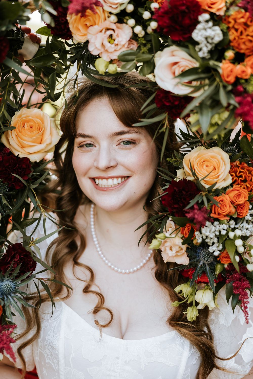A romantic bridal portrait with a floral crown of burgundy and peach blooms against a light background. Cabra Castle