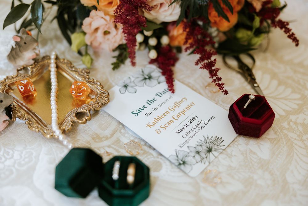 Elegant wedding table setting with velvet ring boxes and floral arrangements in burgundy and emerald green tones. Cabra Castle