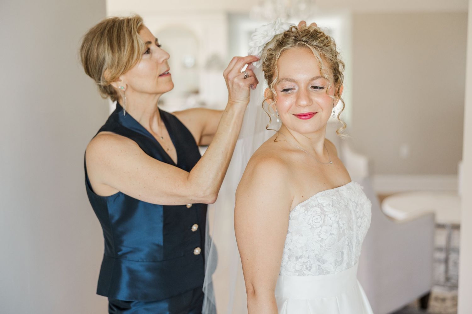 Bride and bridesmaid share joyful laughter during pre-wedding moments in bright indoor setting.