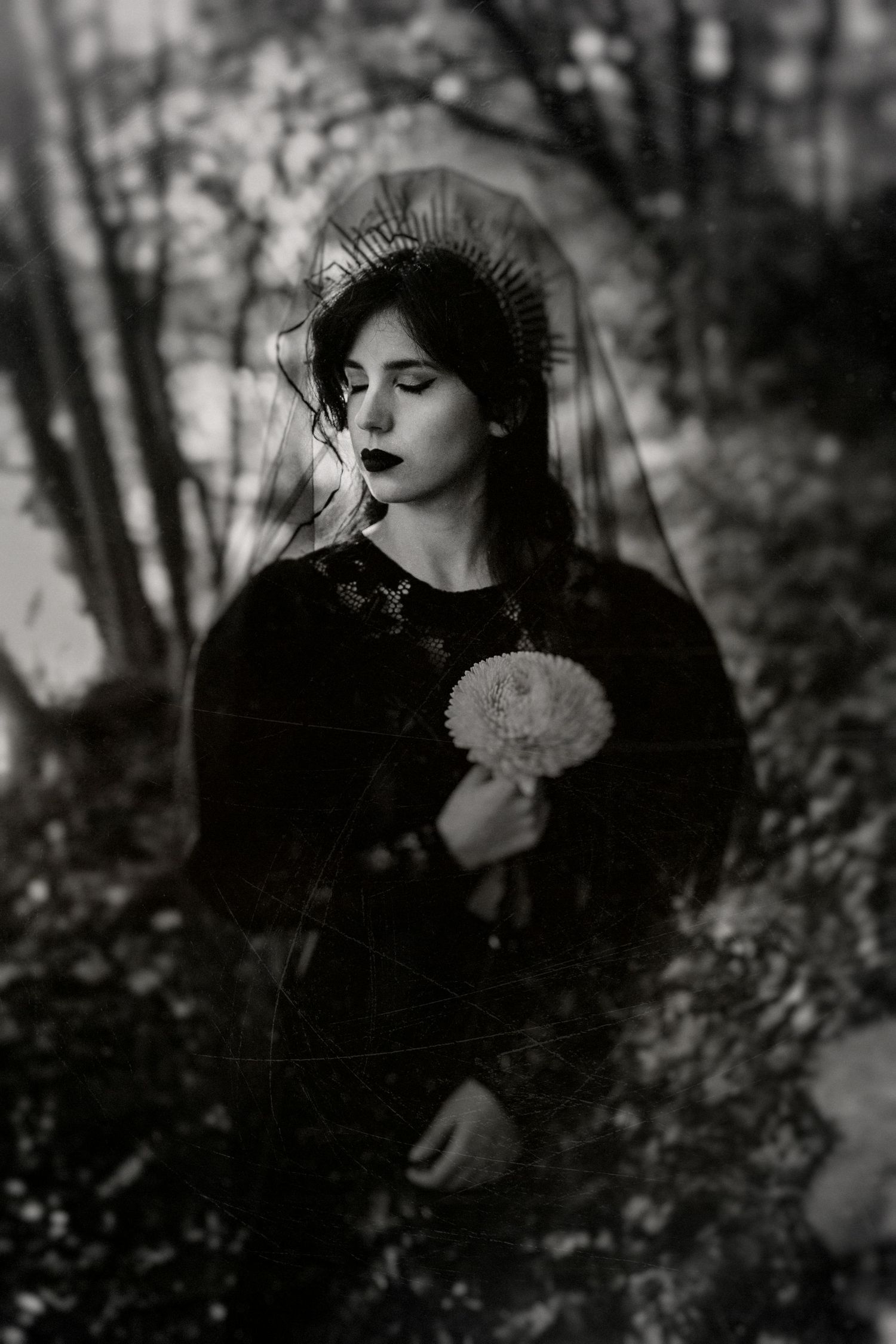 Black and white portrait of a young woman in dark clothing holding a dandelion flower outdoors.