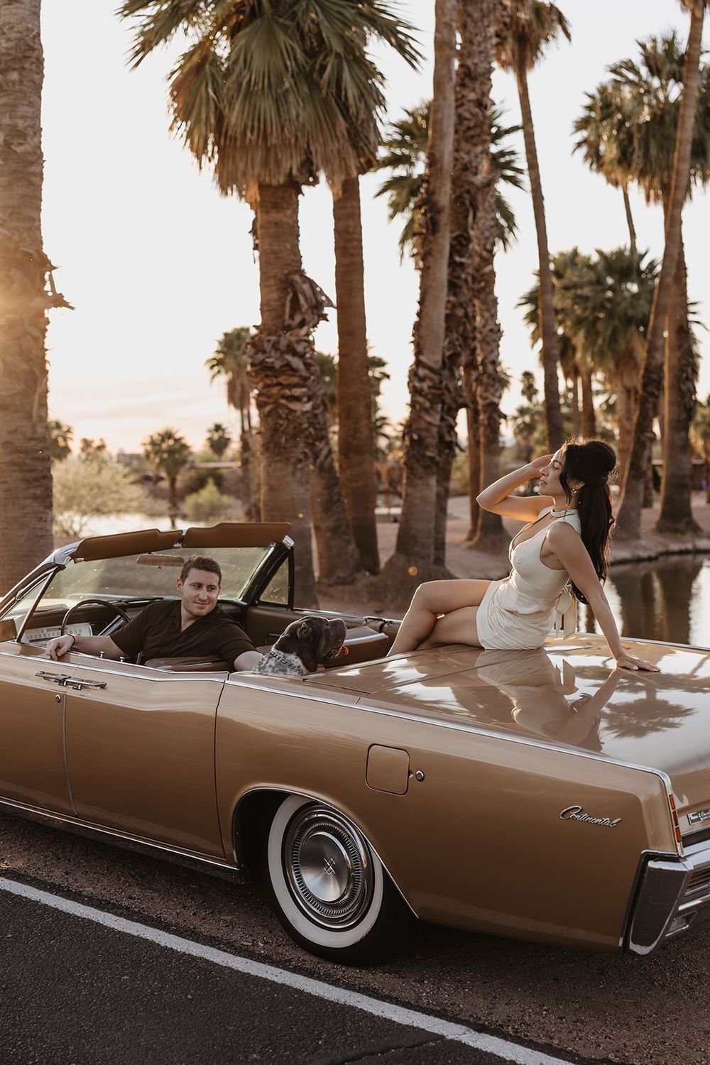 Couple posing with a vintage gold convertible classic car surrounded by palm trees at golden hour sunset.