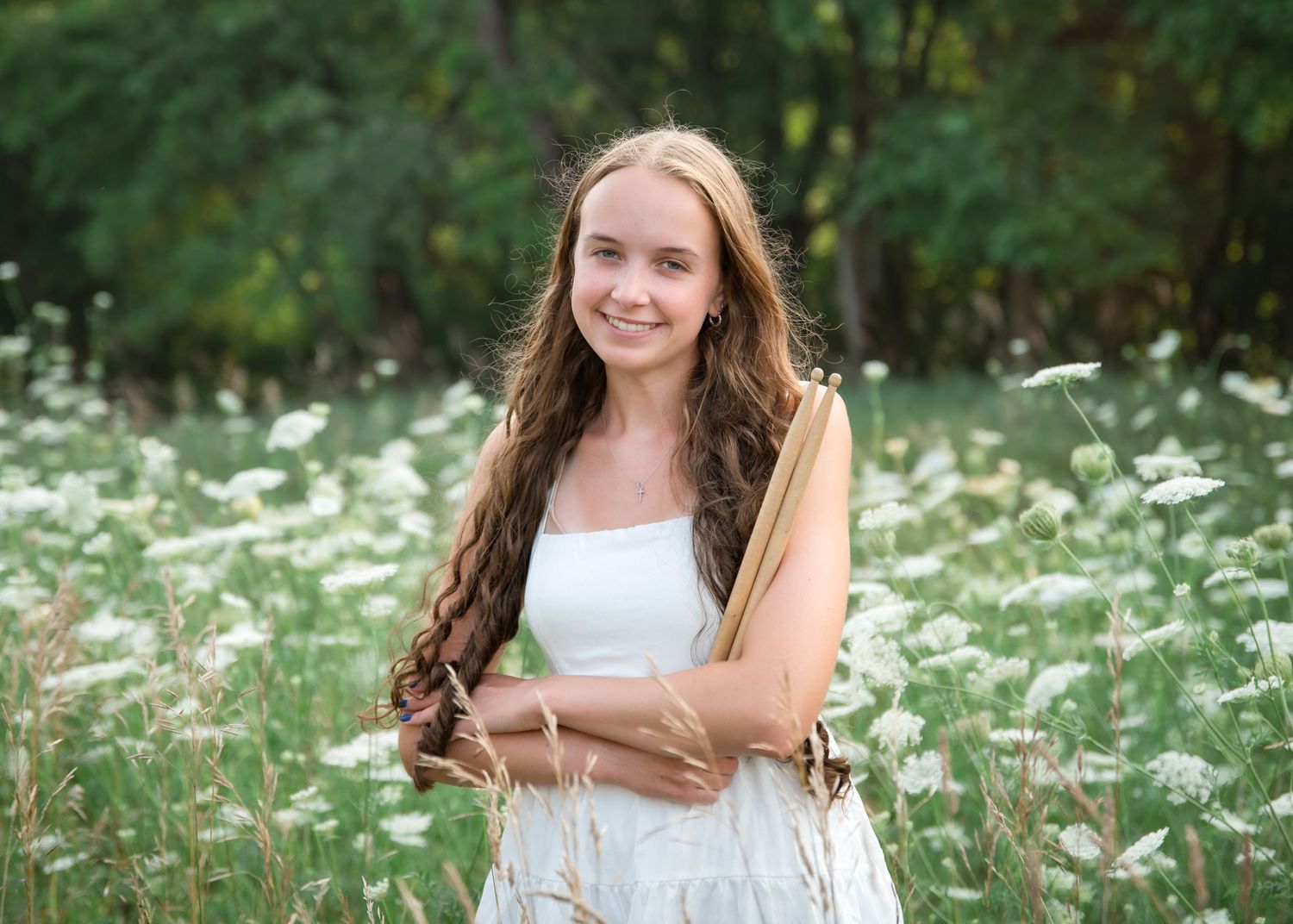 A young woman in a white dress stands in a field of blooming white wildflowers on a summer day.
