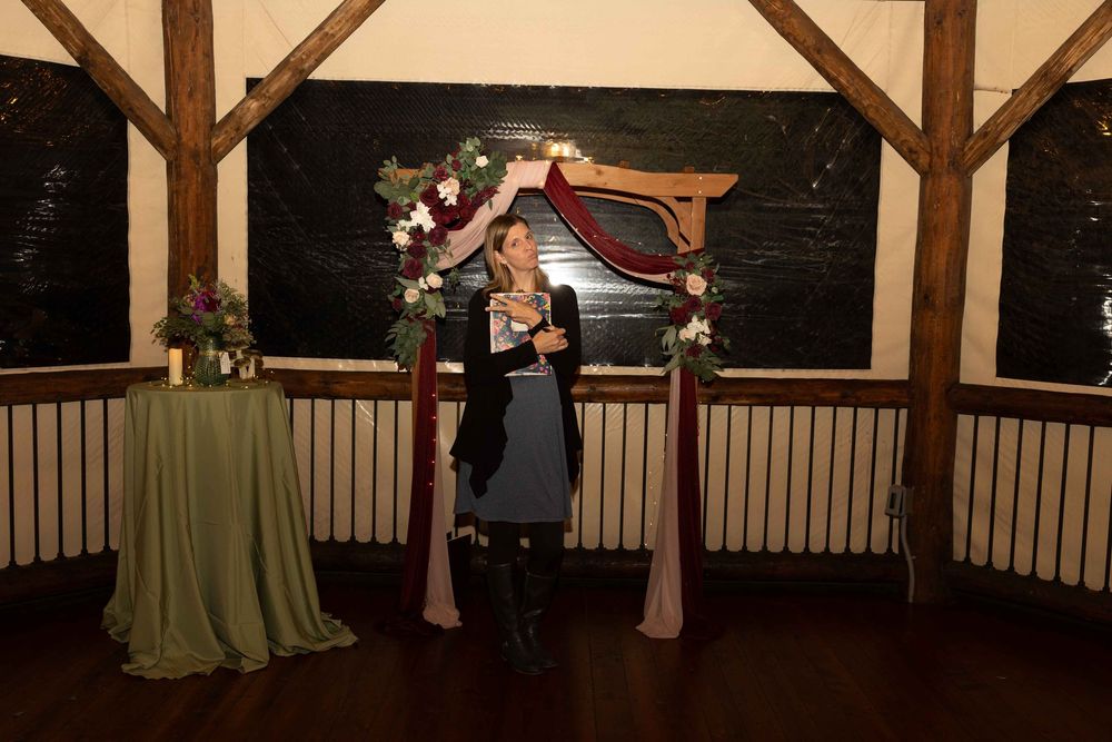 A romantic indoor wedding ceremony setup with a wooden arch decorated with flowers and sage green accents.