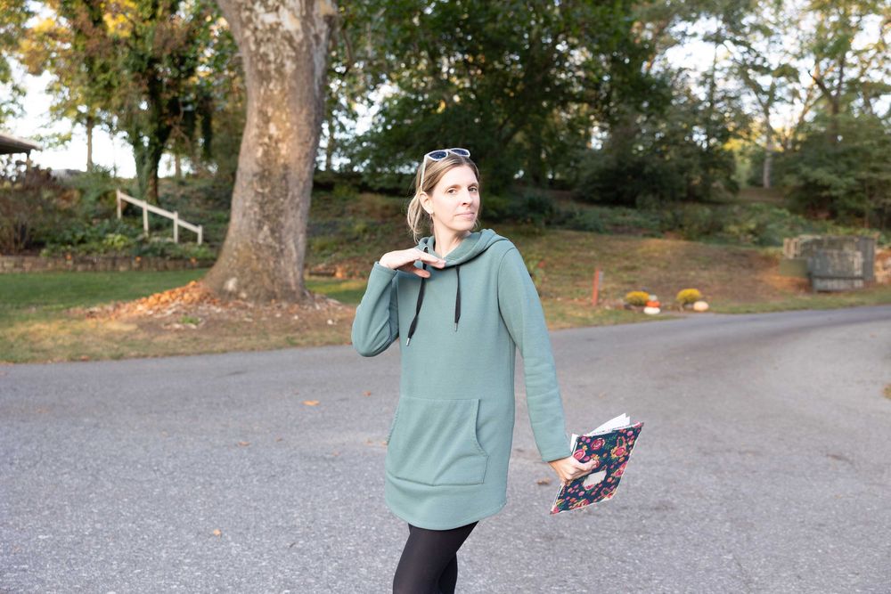 A person in a teal jacket performs a sequence of dance moves in a park setting.