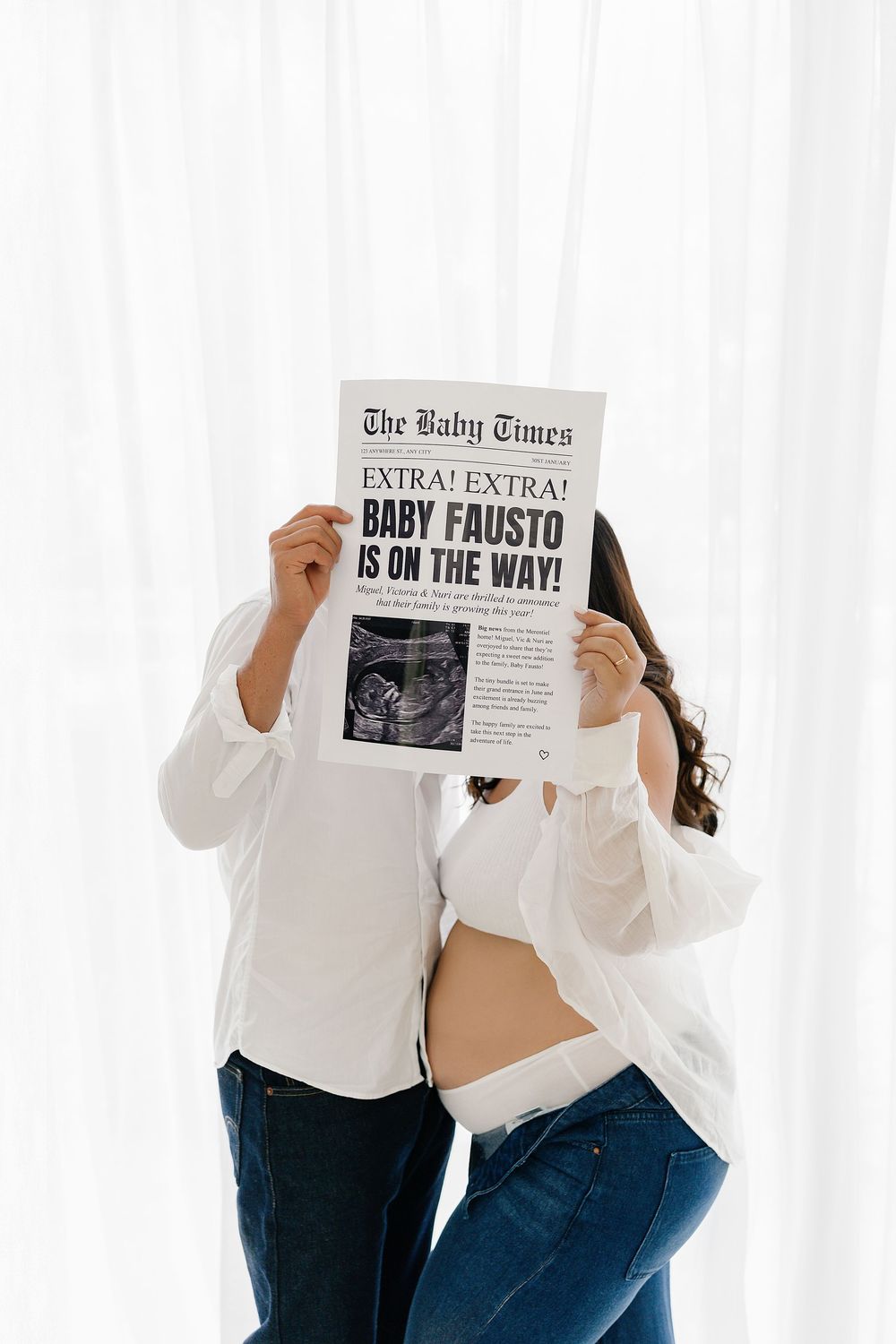 Pregnancy announcement photo with couple holding newspaper headlines reading 'Baby Fausto is on the way' against white backdrop.