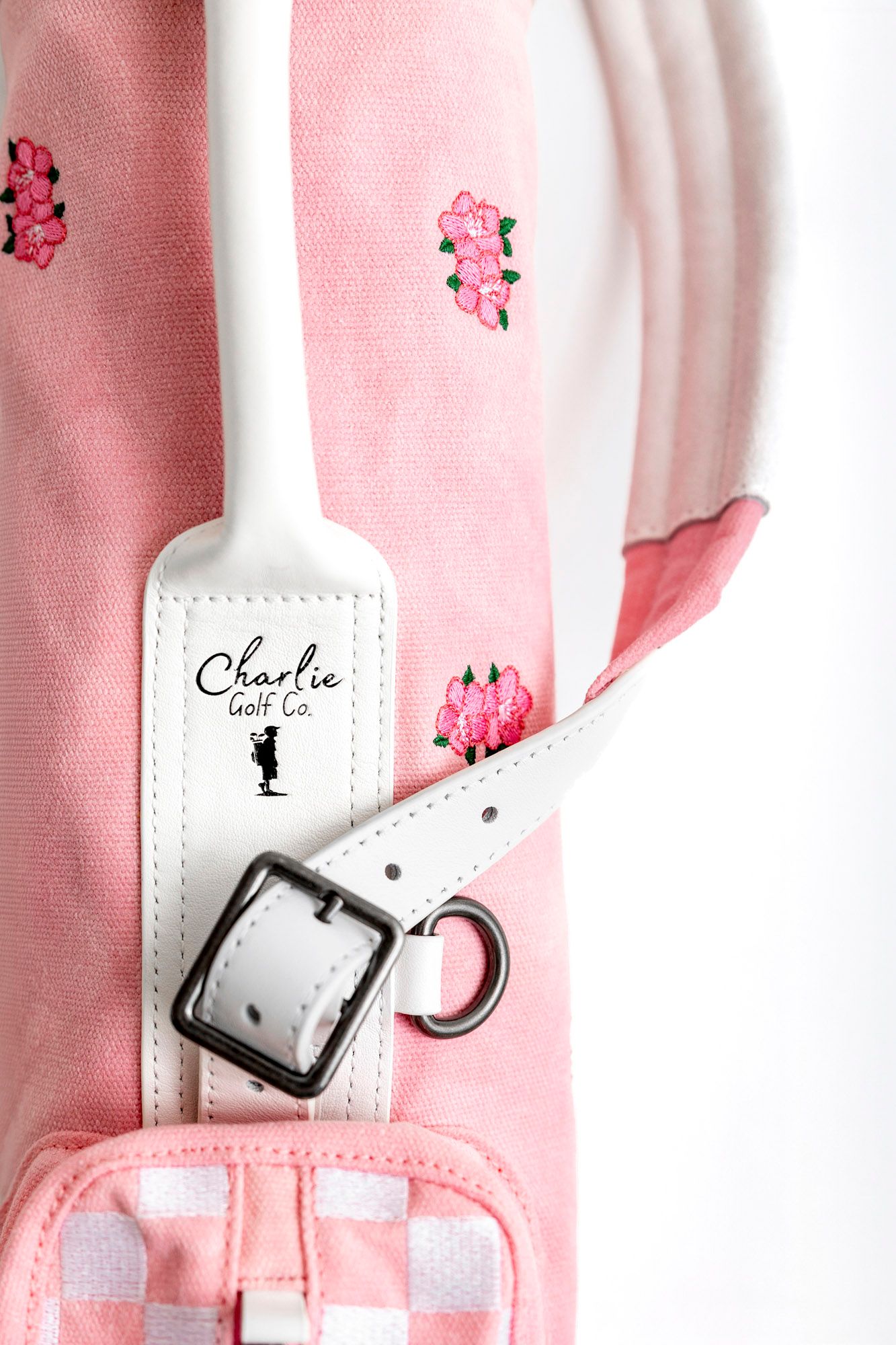 Close-up view of white leather straps with silver buckles on a pink background.