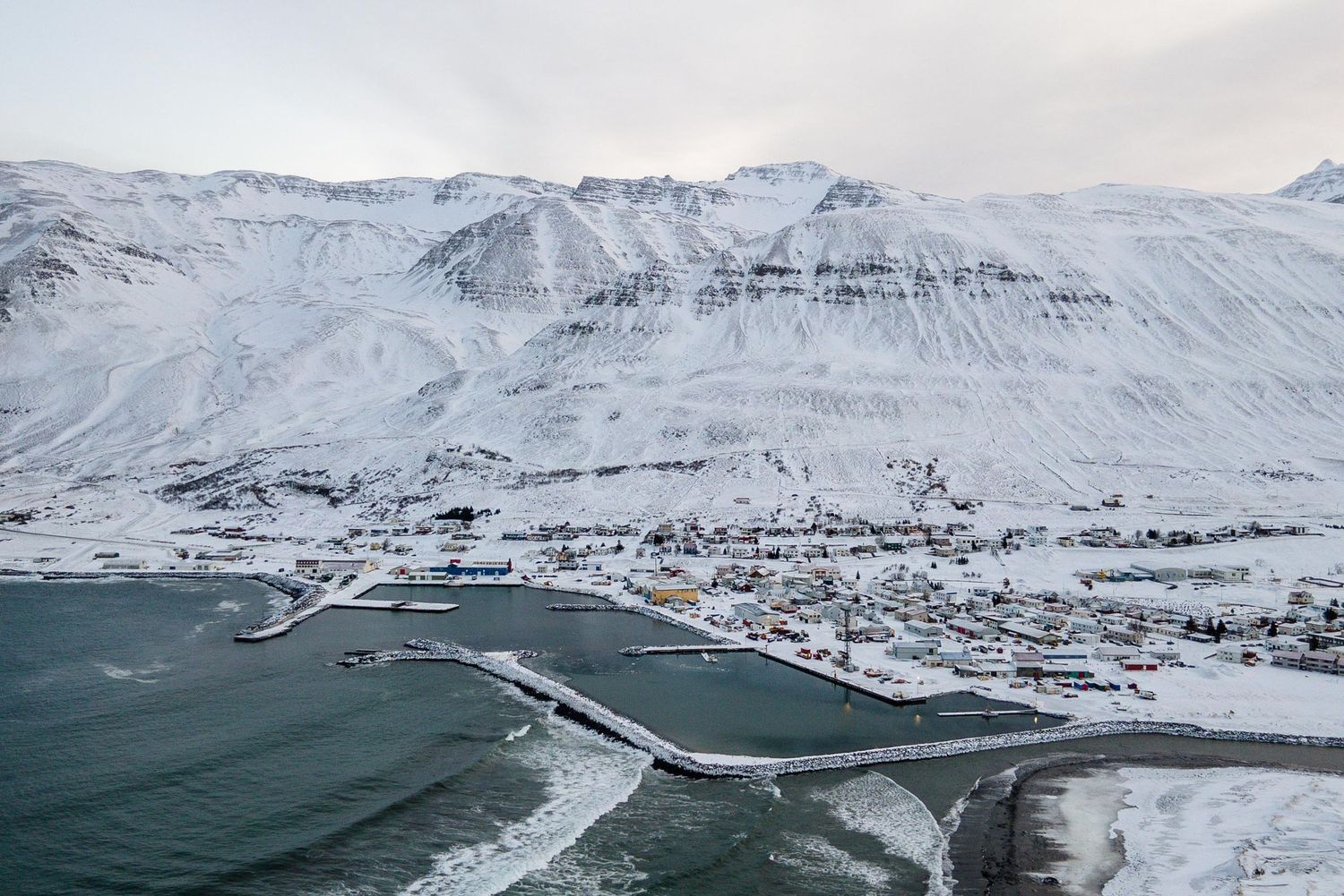 A stunning aerial panorama shows snow-covered mountains surrounding a fjord in Iceland during winter.