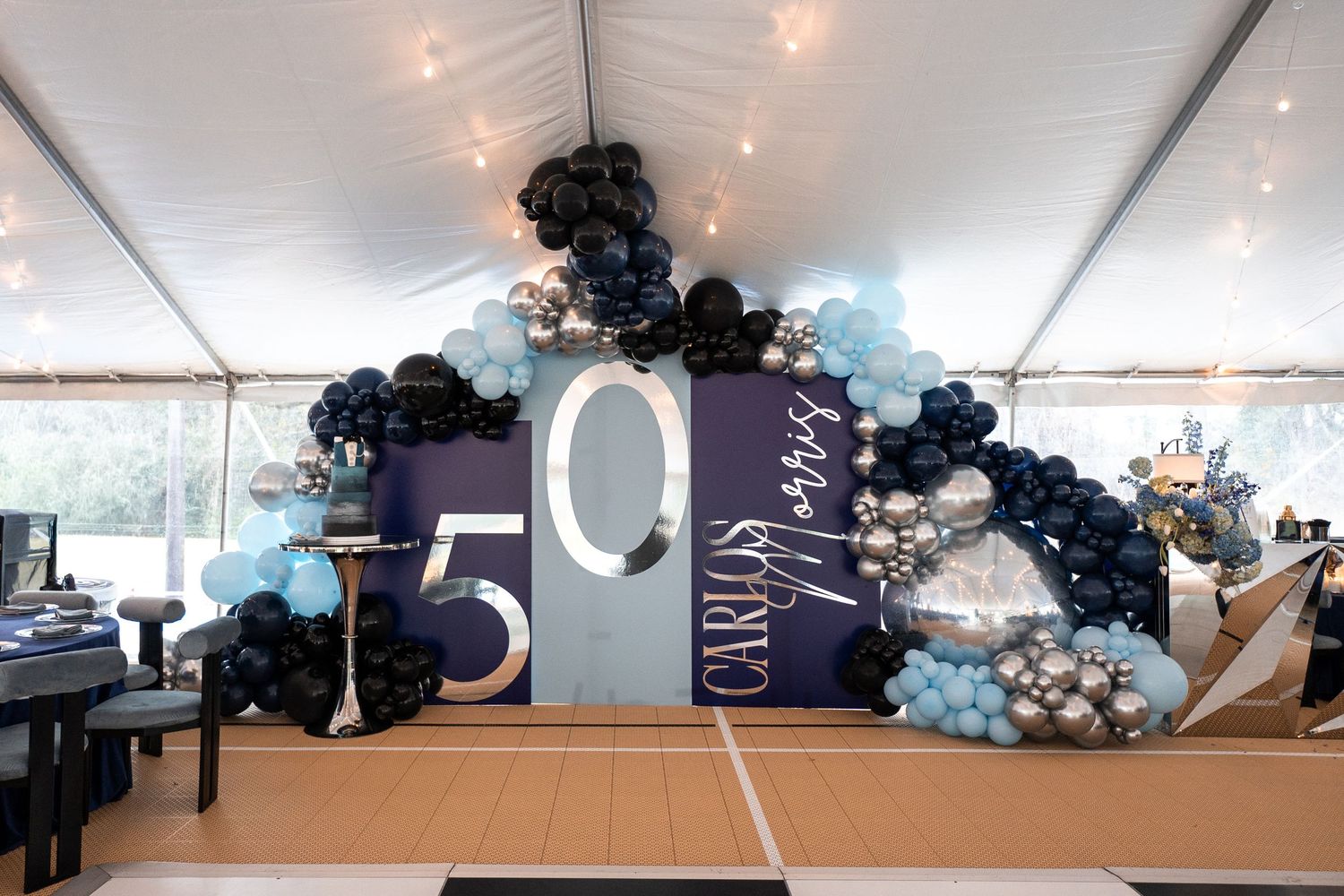 A party venue decorated with elegant blue and white balloon arches and arrangements under a white tent canopy.