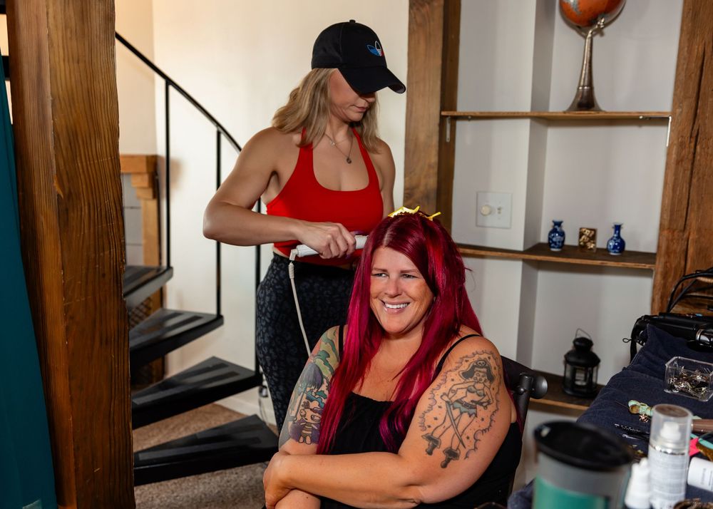 A hairstylist in a red tank top styles the vibrant red hair of a bride at Air BNB in downtown Omaha